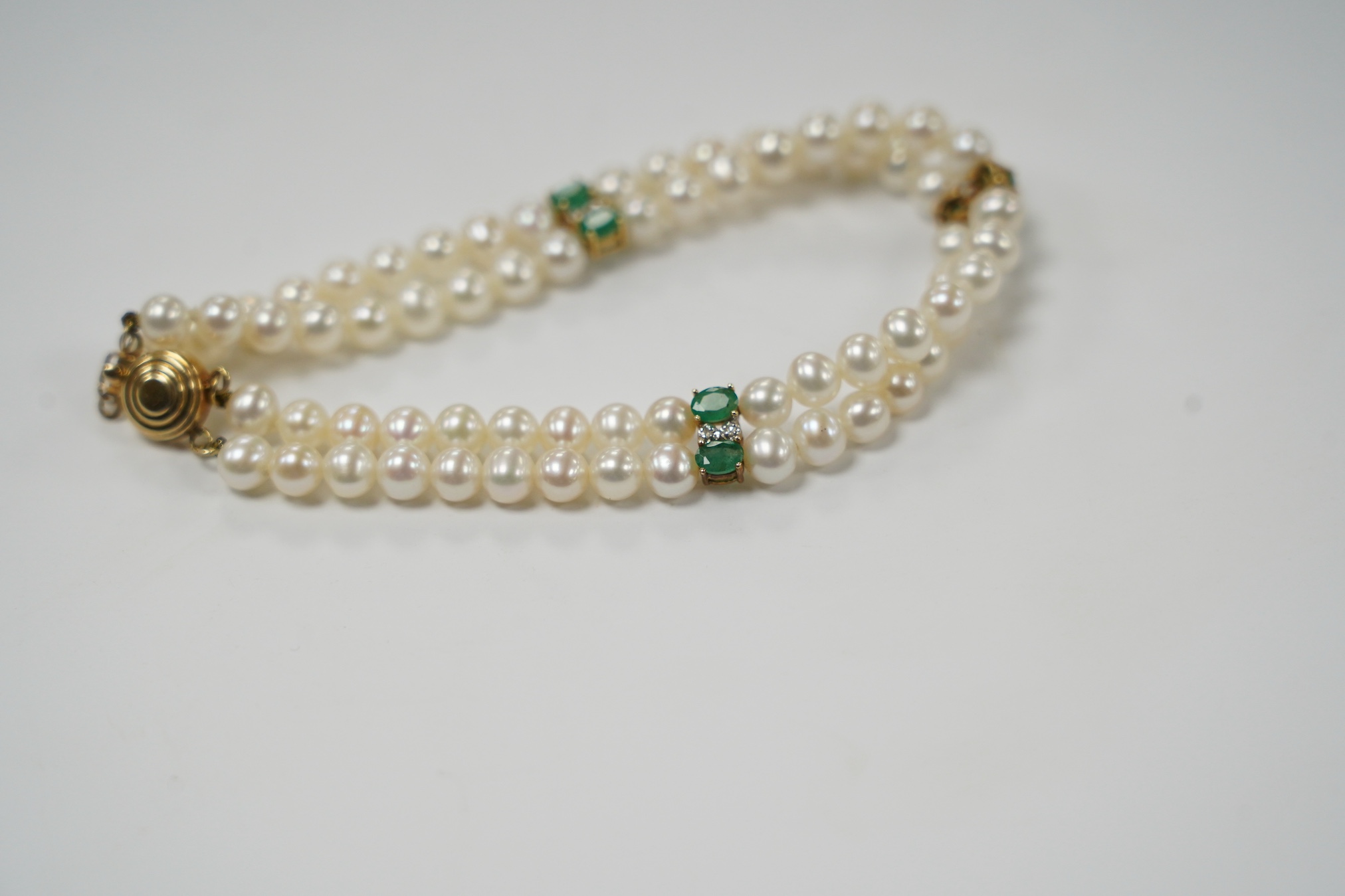 A modern Mexican double strand cultured pearl bracelet, with 14k clasp and emerald and three emerald and diamond cluster set spacers, 17cm. Fair condition.